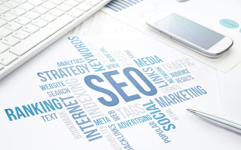 Seo business, search engine optimization, concept cloud chart. Print document, keyboard, pen and smartphone. Blue toned.